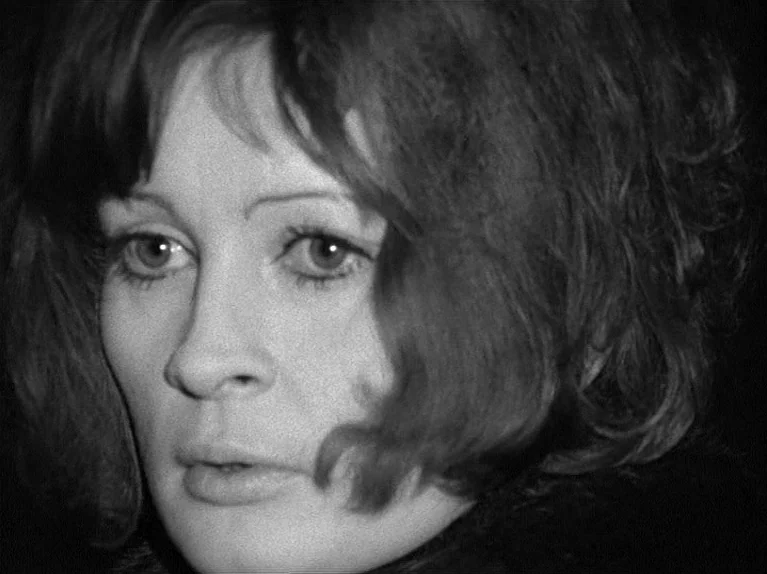 Gods Of The Plague (1970) movie still: closeup — A woman's face is illuminated in a dark, indistinct interior setting. She gazes slightly off-screen…