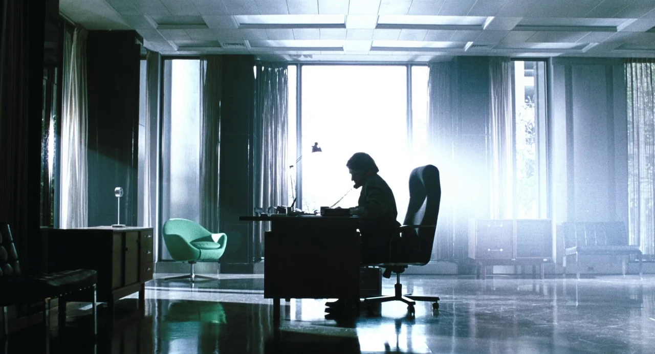 Last Night (1998) movie still: wide — A spacious office features a large desk positioned centrally before floor-to-ceiling windows. A person sits at…