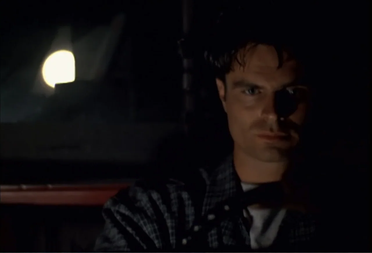 Black Cat Run (1998) movie still: closeup — A dark vehicle interior with a glowing circular light visible in the background. A man sits in the…