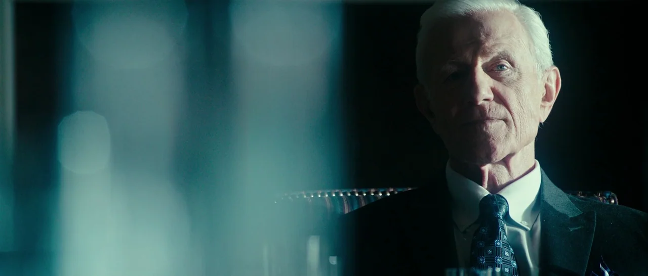 The Purge: Election Year (2016) movie still: closeup — A dimly lit room features a man with white hair seated in a chair. He looks directly forward…