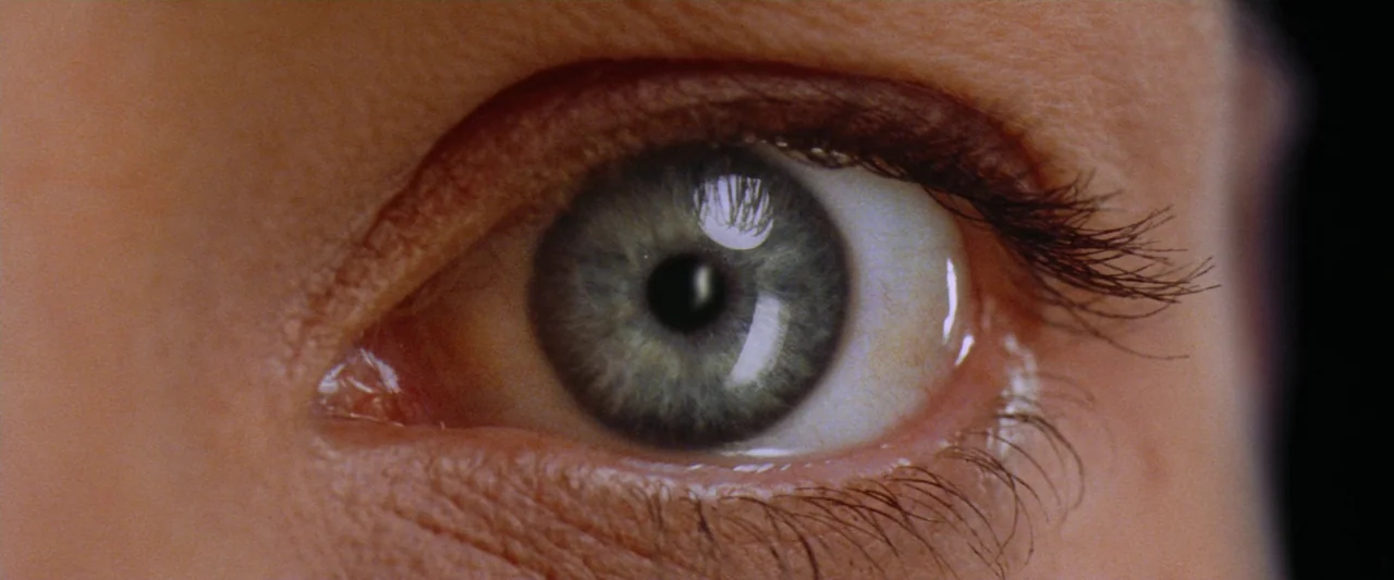 Contact (1997) movie still: closeup — Extreme close-up on a single human eye. The iris shows intricate detail with a reflection of trees visible in…