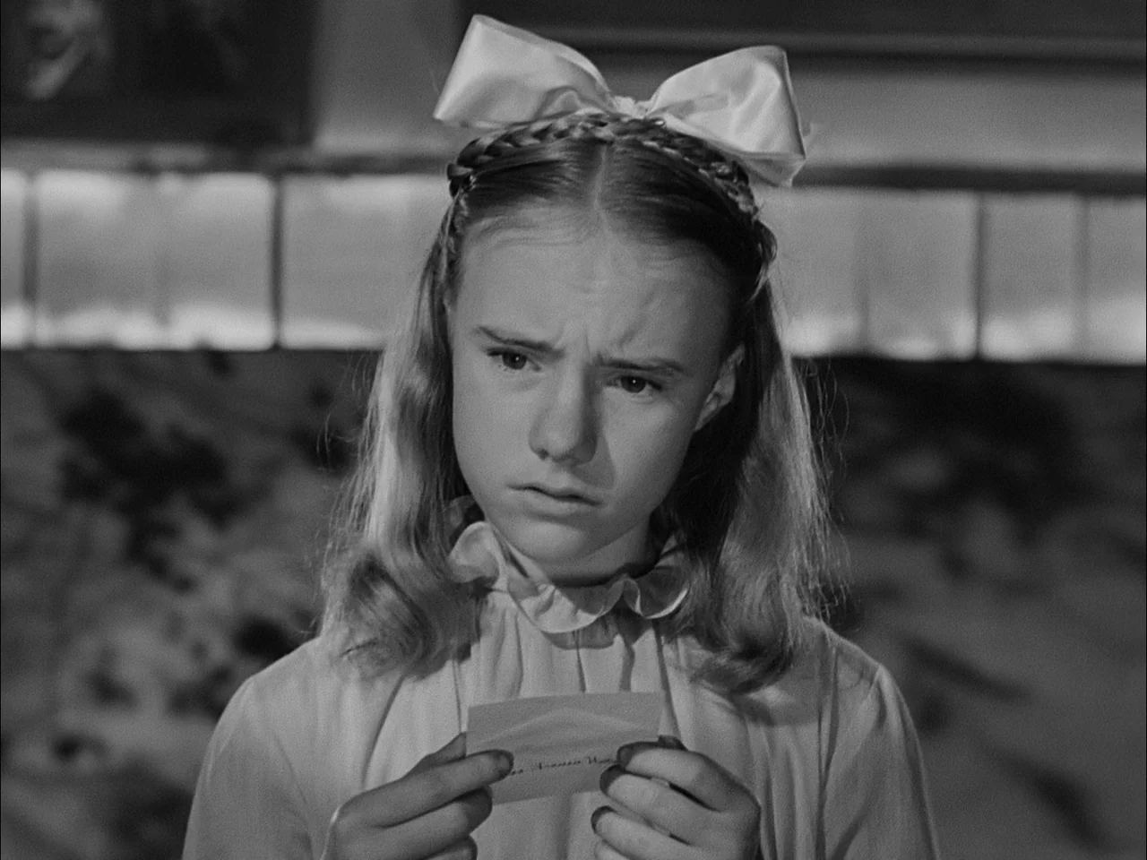A Tree Grows In Brooklyn (1945) movie still: closeup — An interior space features a girl standing in front of a tiled wall. She holds a small,…