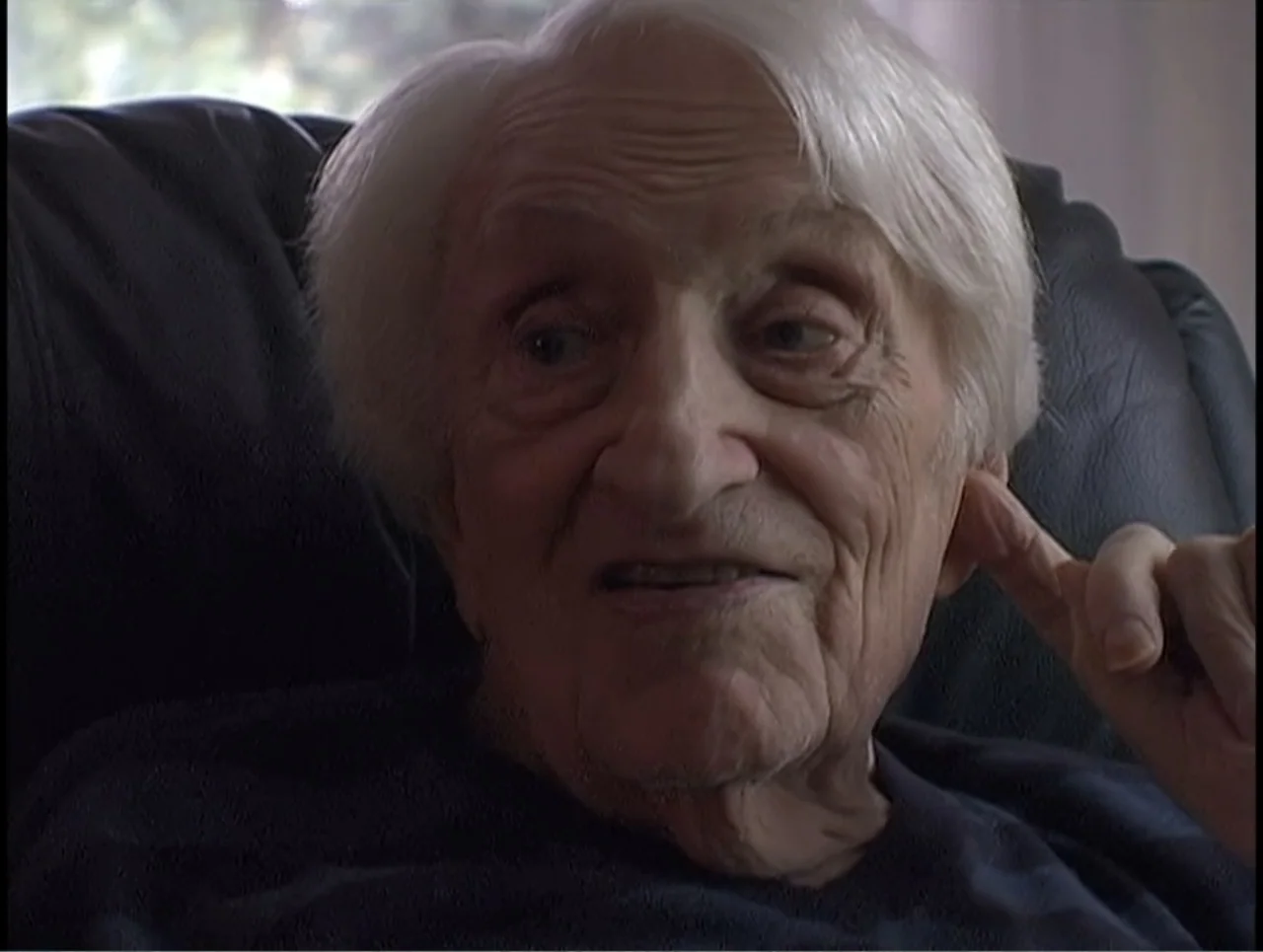 First Cousin Once Removed (2012) movie still: closeup — An elderly person sits in a leather armchair in a residential living room setting. The woman…