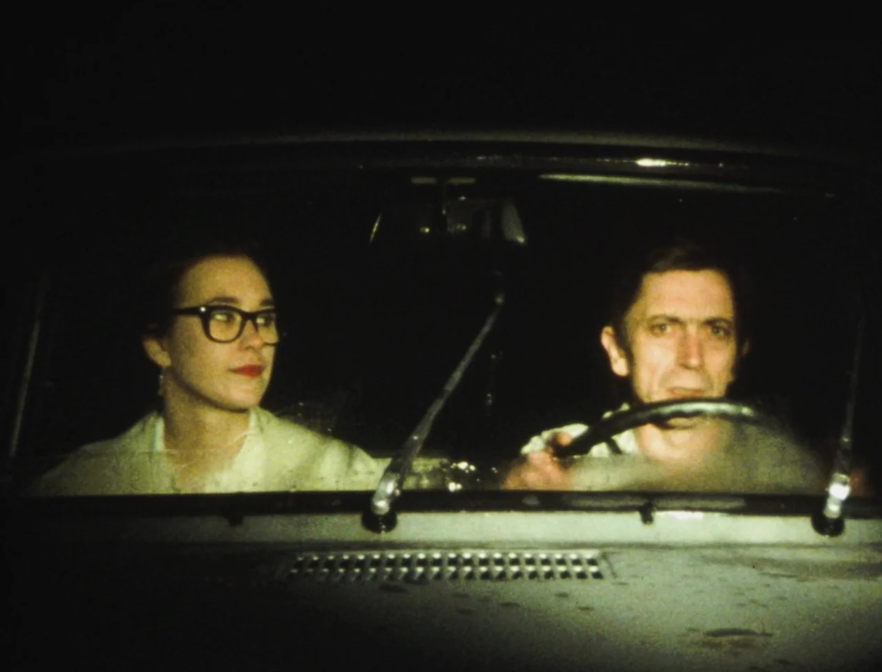 Nekromantik (1988) movie still: medium — The interior of a car at night seen from the passenger perspective. A man drives and a woman looks toward…