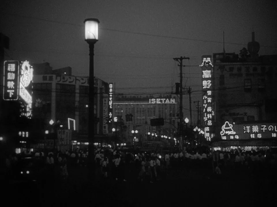 Godzilla (1954) (1954) movie still: establishing — A bustling street corner in post-war Japan filled with illuminated neon commercial signage.…