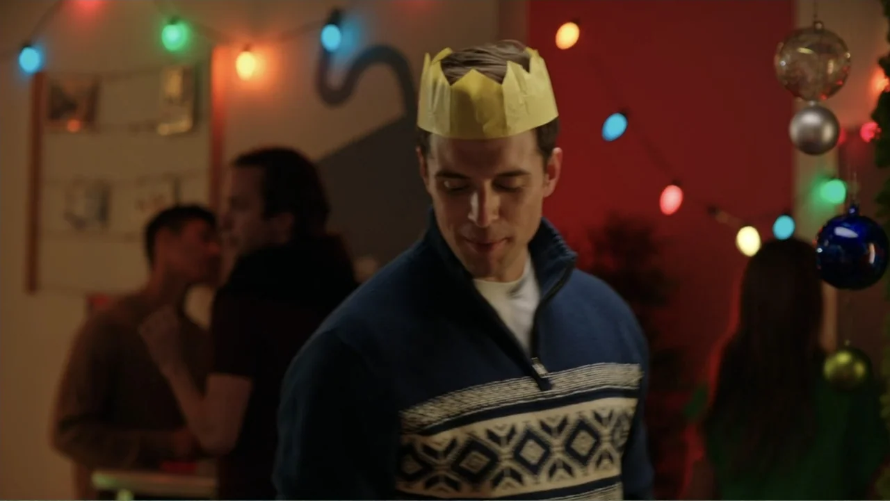 Ghosts of Christmas Past (2021) movie still: medium — A festive indoor social gathering features holiday string lights hung against a plain wall. A…