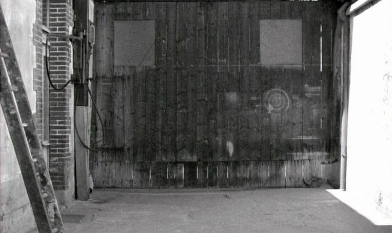 Jacquot de Nantes (1991) movie still: establishing — A narrow alleyway features a large, weathered wooden gate set against brick walls. A wooden…
