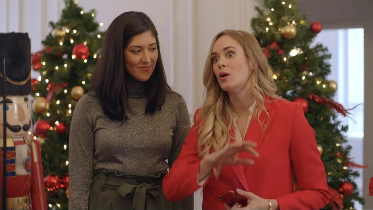 Loving Christmas (2022) movie still: medium — A living room interior features two decorated Christmas trees and a large nutcracker statue. Two women…