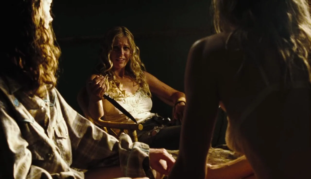 The Devil’s Rejects (2005) movie still: medium — A dimly lit room with dark surroundings isolates the three individuals present. A woman with blonde…