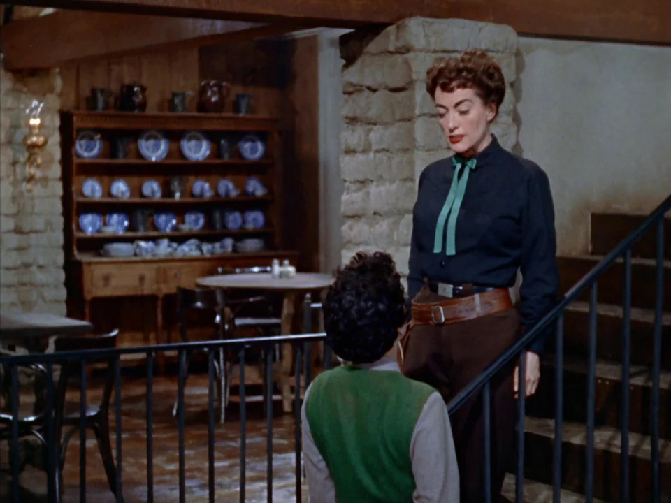 Johnny Guitar (1954) movie still: medium — An interior room features stone pillars, a wooden staircase, and a china cabinet display. A woman stands…