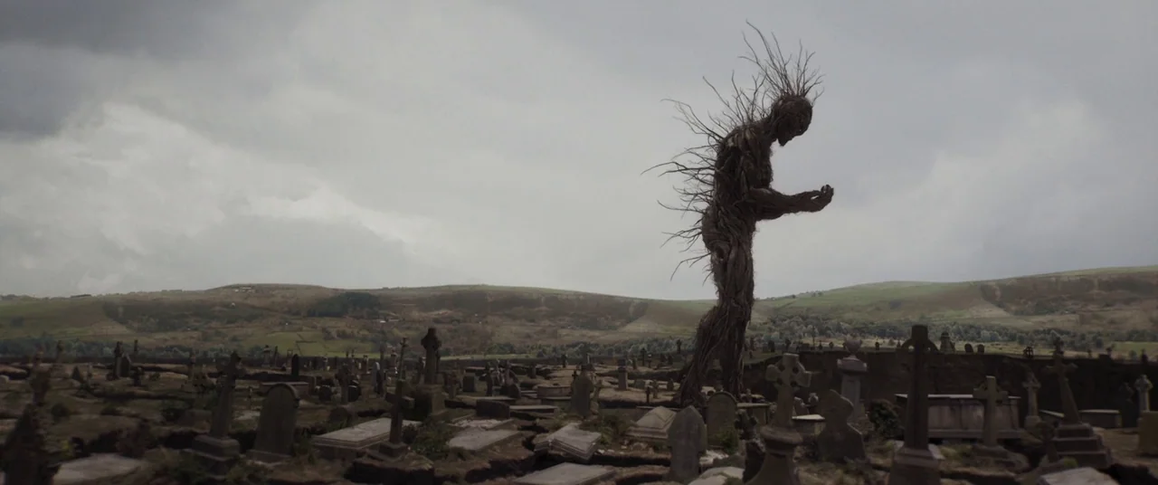 A Monster Calls (2016) movie still: wide — An expansive cemetery features rows of weathered headstones under a heavy, overcast cloudy sky. A…