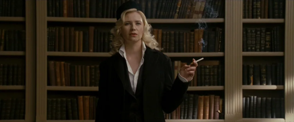 The Brothers Bloom (2008) movie still: medium — A room with tall built-in wooden shelves packed with many leather-bound vintage books. A woman in a…