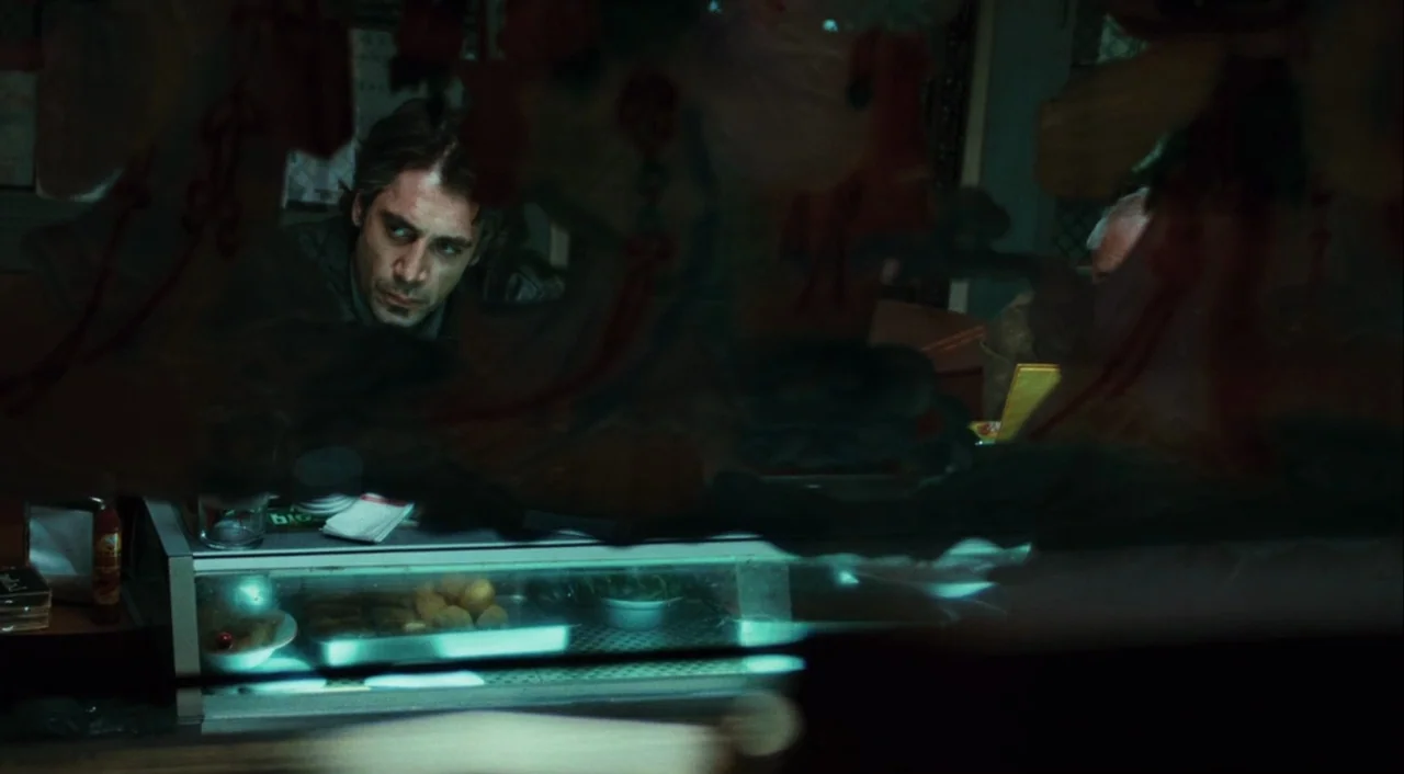 Biutiful (2010) movie still: medium — A dimly lit counter area features a glass display case with food items inside. A man leans against the counter…