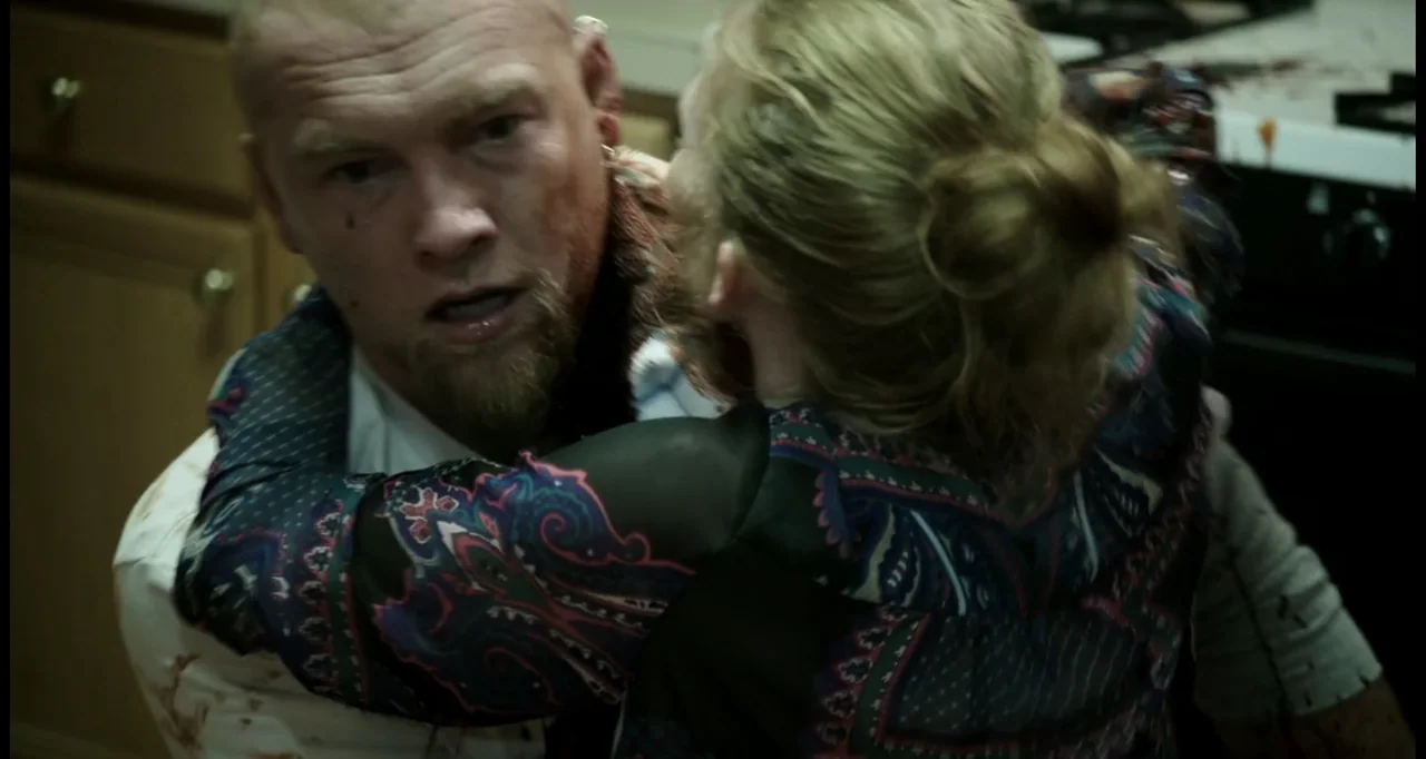 Sabotage (2014) movie still: medium — A residential kitchen featuring wooden cabinetry and a tiled countertop area. A man and a woman stand locked…
