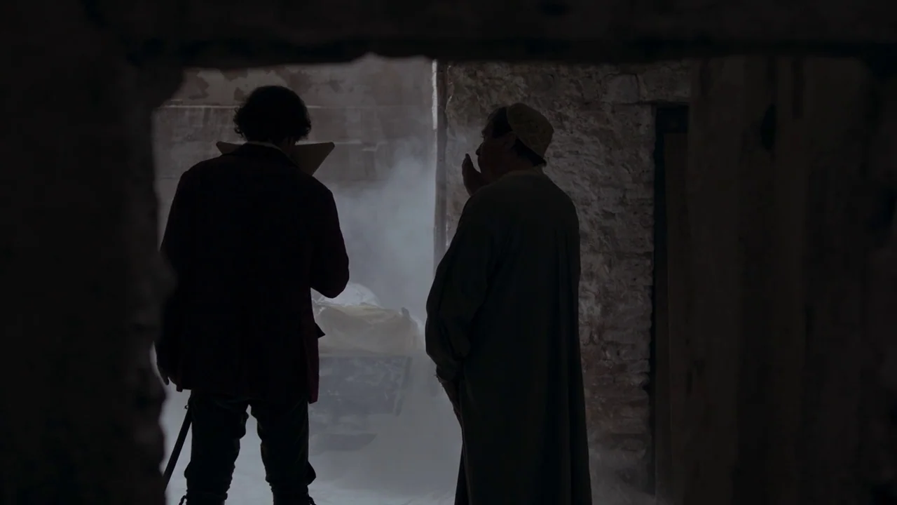 Zama (2017) movie still: medium — A dark, stone-walled cellar room filled with thick, swirling white smoke. Two men stand in the foreground,…