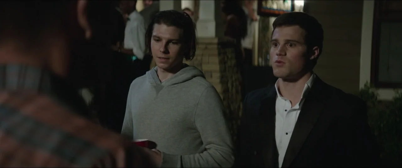 Blockers (2018) movie still: medium — Two men stand on a residential porch at night during a social gathering. They look toward a person off-screen…