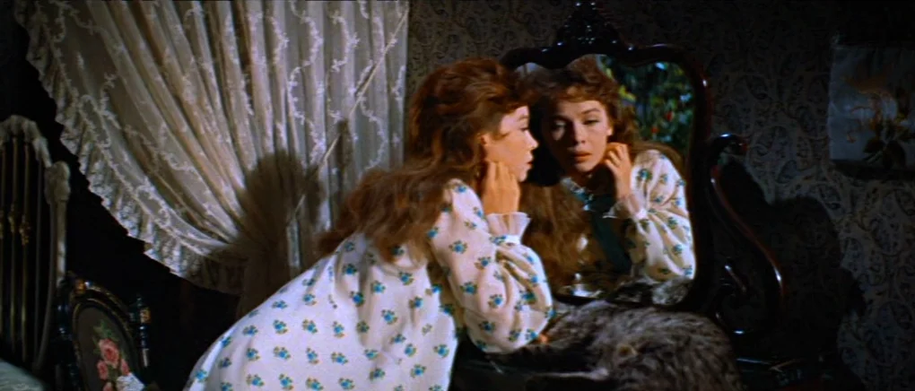 Gigi (1958) movie still: medium — A dimly lit room contains an ornate wooden vanity mirror placed against patterned wallpaper. A young woman in a…