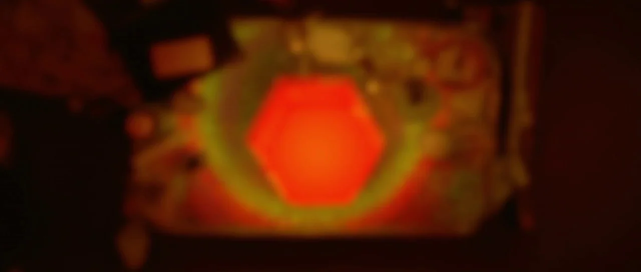 Enter The Void (2009) movie still: closeup — A blurred abstract environment is dominated by a central glowing hexagonal light source. The light…