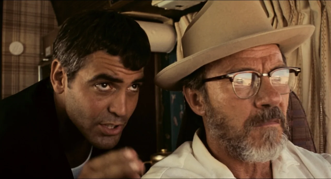 From Dusk Till Dawn (1996) movie still: medium — The interior of a van features plaid upholstery and beige curtains near the window. One man leans…