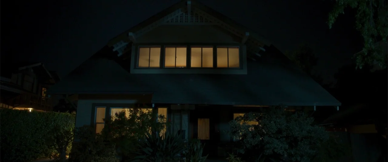 Phobias (2021) movie still: wide — A two-story suburban house stands in total darkness at night. Warm interior light leaks from the upper and lower…