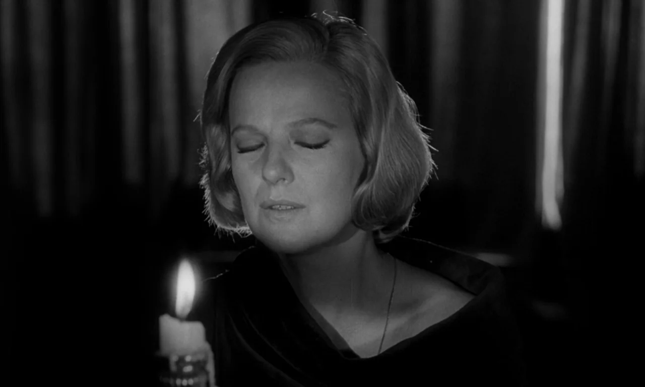 Seance on a Wet Afternoon (1964) movie still: closeup — A dark room with heavy curtains visible in the background shadows. A woman stands with her…
