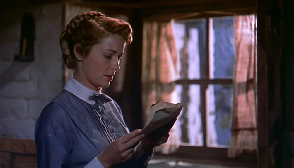 The Searchers movie still: medium — A rustic room features white-washed stone walls and a wooden window frame with curtains. A woman stands in front…