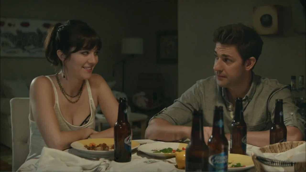 The Hollars (2016) movie still: medium — A dimly lit residential dining area features a table set for two people. A man and a woman sit facing each…