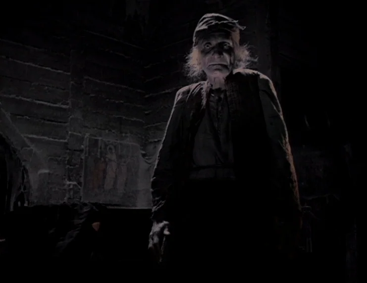 Viy (1967) movie still: medium — A dark, dilapidated room features wooden walls with a faded religious icon hanging nearby. An elderly, gaunt man…