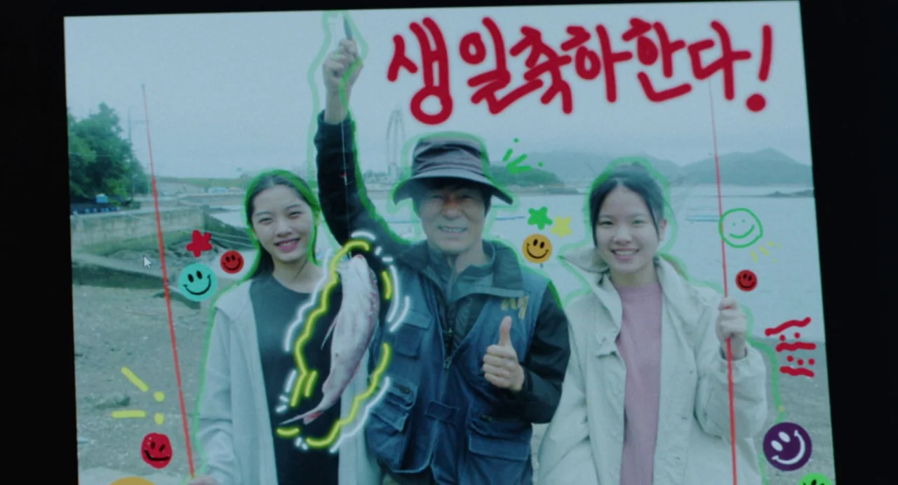 Return To Seoul (2022) movie still: medium — A man stands between two young women on a waterfront while holding a fish. The image is overlaid with…