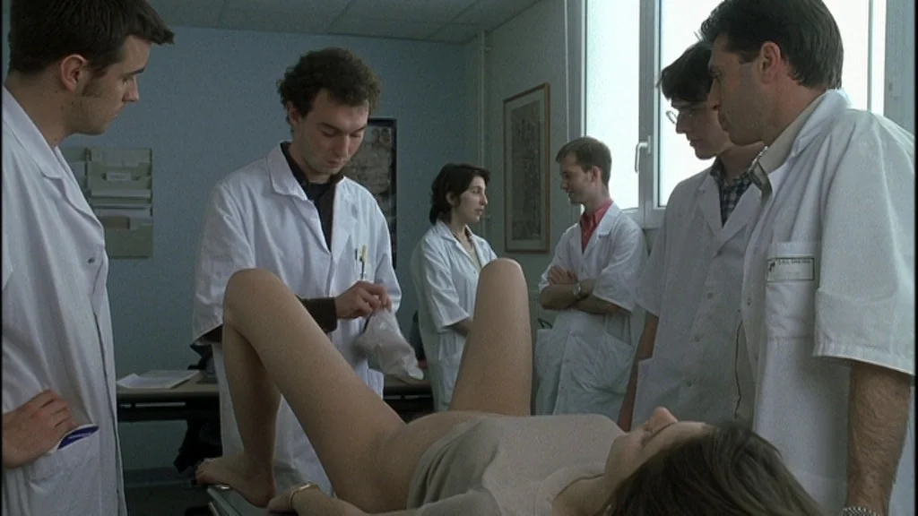 Romance (1999) movie still: medium — A clinical examination room features white walls and a large, bright window. Medical staff in white lab coats…