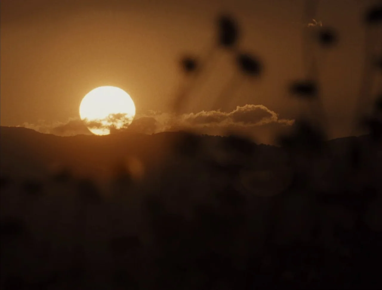 Christ Stopped at Eboli (1979) movie still: establishing — A bright sun descends behind a dark, silhouetted mountain range at dusk. Out-of-focus…