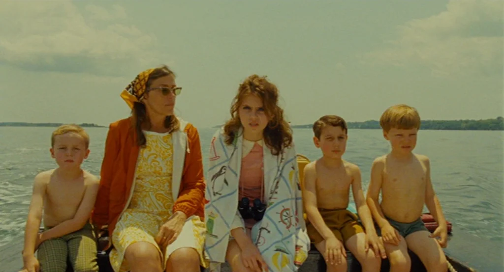 Moonrise Kingdom (2012) movie still: medium — A group of five people sit together on a small boat during the day. They face the camera against the…