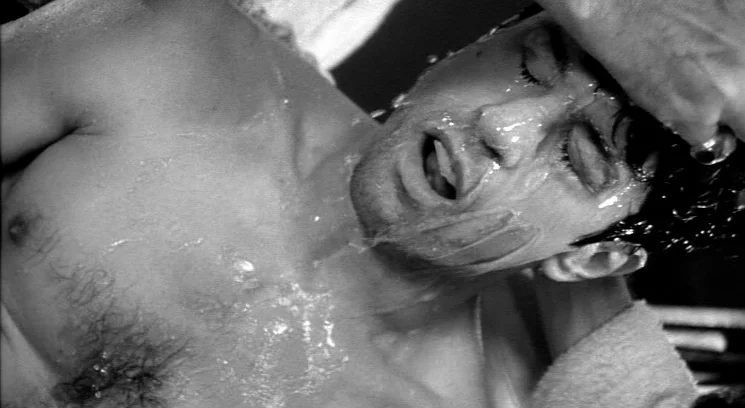 Raging Bull (1980) movie still: closeup — A man lies on a tiled surface in a dimly lit bathroom area. Water covers his chest and face while his eyes…