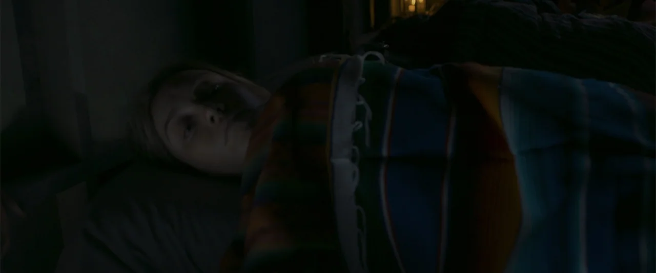 Mirreyes contra Godínez 2: El retiro (2022) movie still: closeup — A dark bedroom interior with a person resting under a woven striped blanket. The…