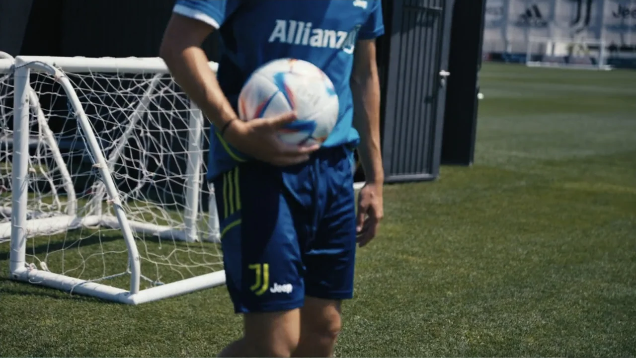Federico Chiesa - Back on Track (2023) movie still: medium — A sunny outdoor soccer practice field features a portable goal frame. A male athlete in…