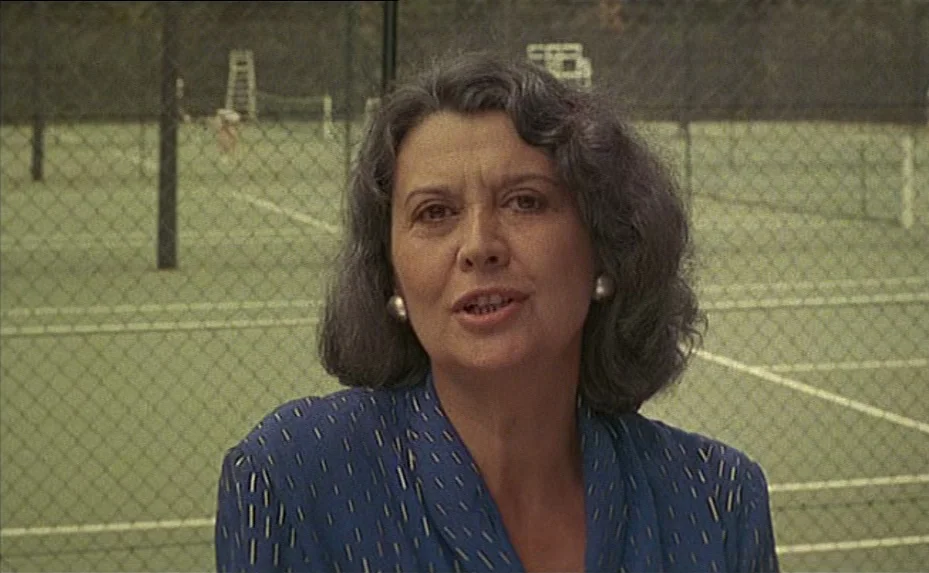The Woman Next Door (1981) movie still: medium — A tennis court with chain-link fencing serves as the backdrop for the woman. A middle-aged woman in…