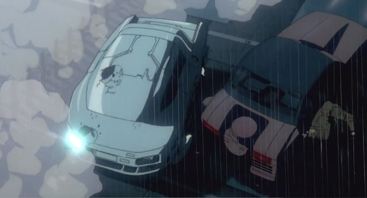 Ghost in the Shell (1995) movie still: wide — A high-angle view shows two cars parked on a dark wet road during rain. A man in an olive jacket…