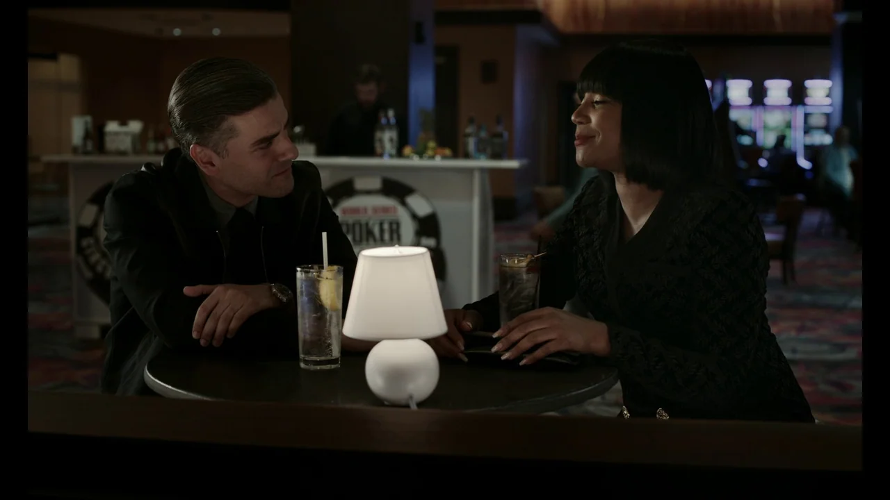 The Card Counter (2021) movie still: medium — A dimly lit casino area features a round table with a small glowing lamp. A man and a woman sit…