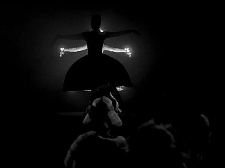 My 20th Century (1989) movie still: medium — A dark performance area contains a single female figure illuminated from behind. She holds a dance pose…