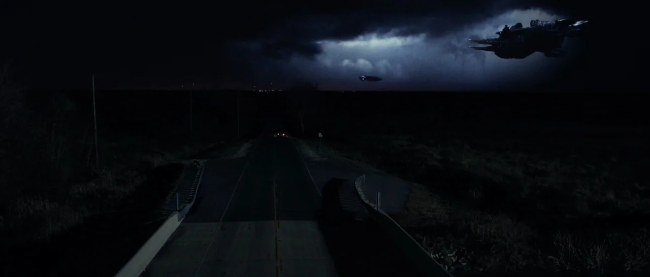 10 Cloverfield Lane (2016) movie still: establishing — A dark rural road stretches toward a horizon beneath a stormy, overcast night sky. Two…