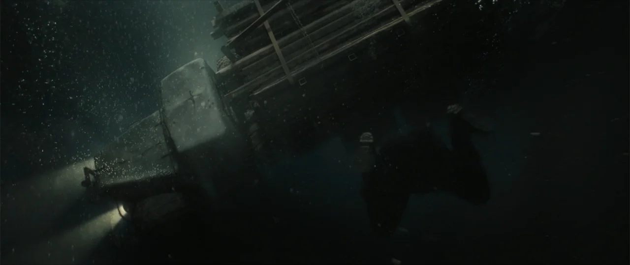 Sisu: Road to Revenge (2025) movie still: wide — A massive transport truck is partially submerged in deep, murky water at night. The vehicle's…