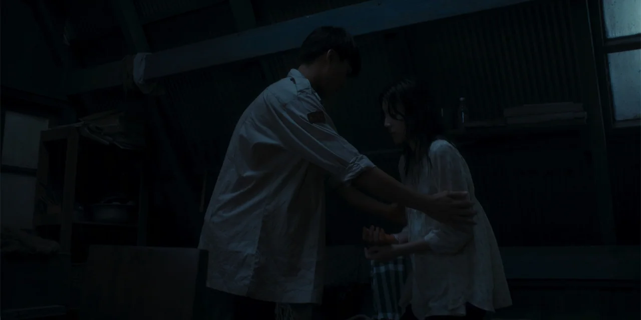Host (2020) movie still: medium — A dark, cramped attic features exposed wooden beams and a corrugated metal roof. A man reaches out to steady a…