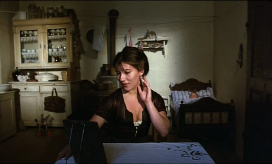 Woyzeck (1979) movie still: medium — A dimly lit room with simple wood furniture and a rustic, lived-in aesthetic. A young woman sits at a table…