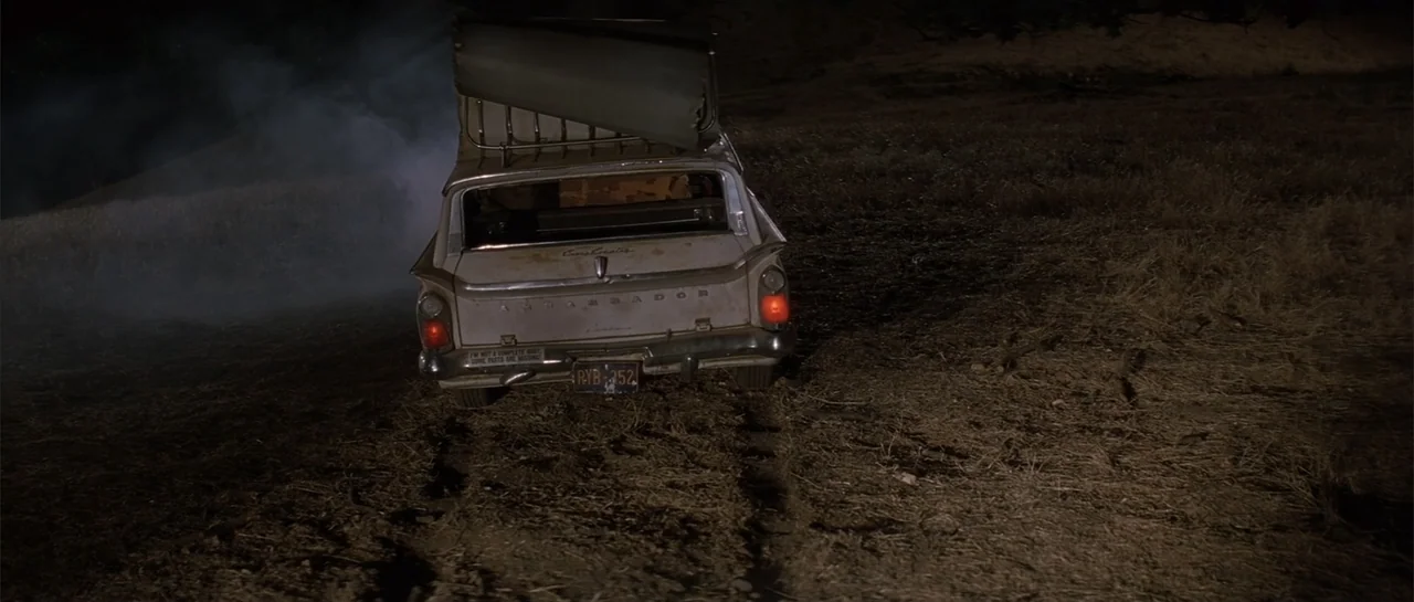 Jeepers Creepers 2 (2003) movie still: wide — A vintage station wagon sits stalled in a dark, barren field at night. Thick smoke rises from the rear…