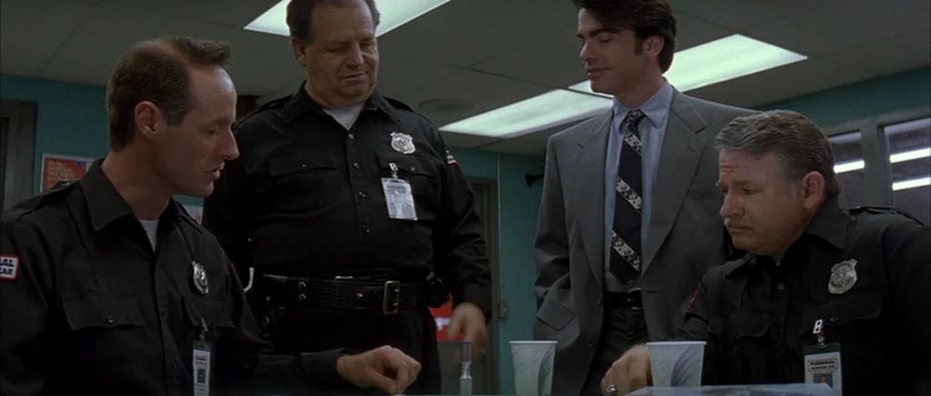 The Underneath (1995) movie still: medium — A utilitarian security room features drop-ceiling panels and teal wall paint. Four men in professional…