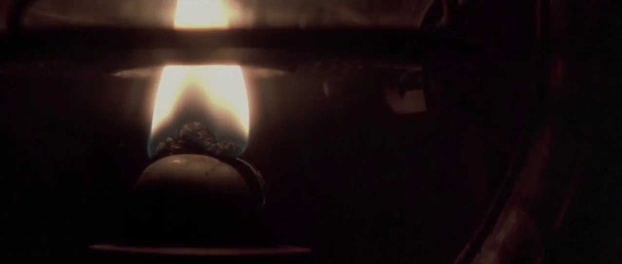 Snow Falling on Cedars (1999) movie still: closeup — Close-up of a burning wick inside the glass housing of an old oil lamp. The surrounding space…