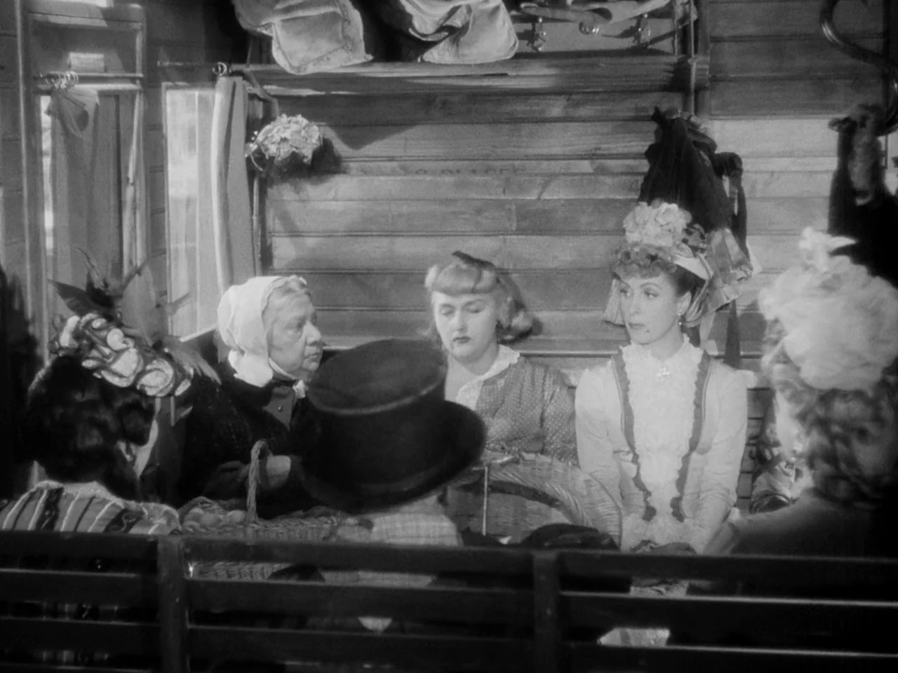 Le Plaisir (1952) movie still: medium — A wooden train carriage interior with passengers seated in facing rows. Several women wearing…