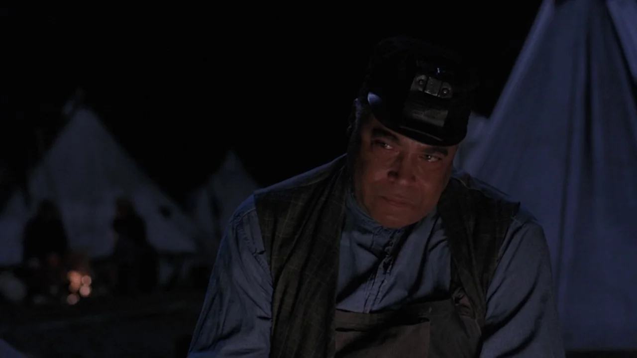 Matewan (1987) movie still: medium — An nighttime military encampment features multiple white canvas tents in the soft darkness. A man in a work…