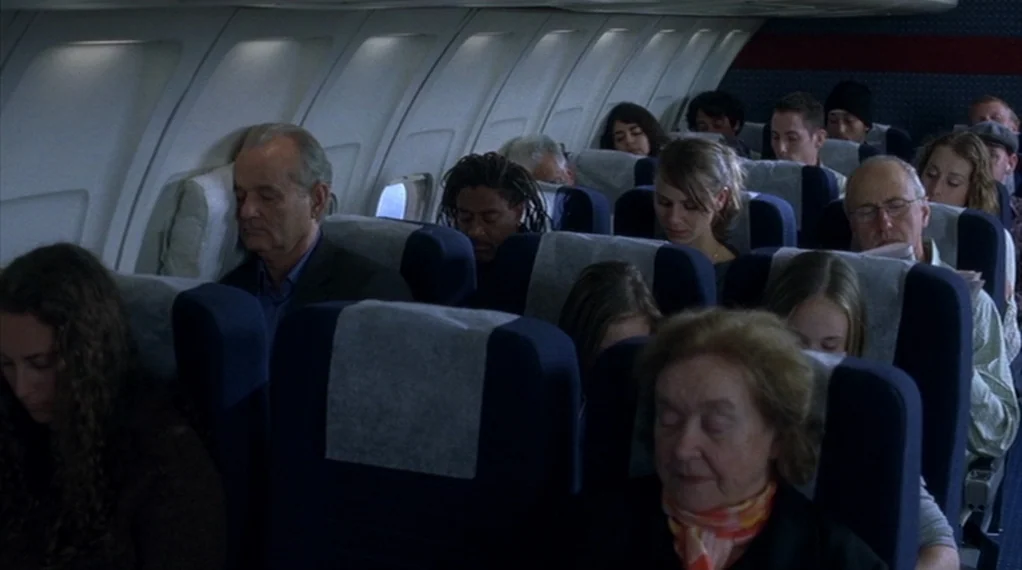 Broken Flowers movie still: medium — The interior of a commercial airplane cabin shows multiple passengers asleep in their seats. Most individuals…