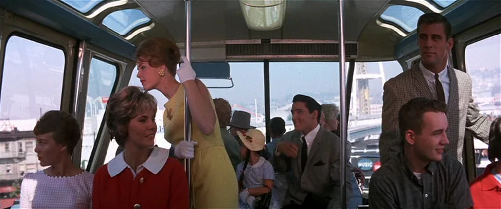 It Happened At The World’s Fair (1963) movie still: medium — A group of passengers rides inside a brightly lit vintage cable car with large windows.…